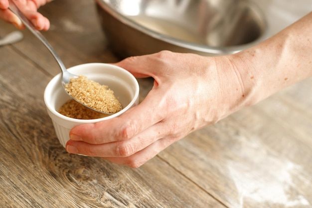 Hand holding a small bowl of powdered gelatin with a spoon over a wooden surface.